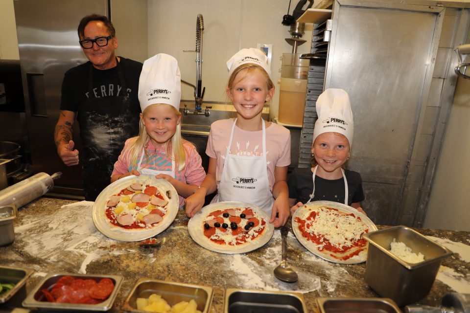 three children pose with a chef in a restaurant kitchen after making their own pizzas