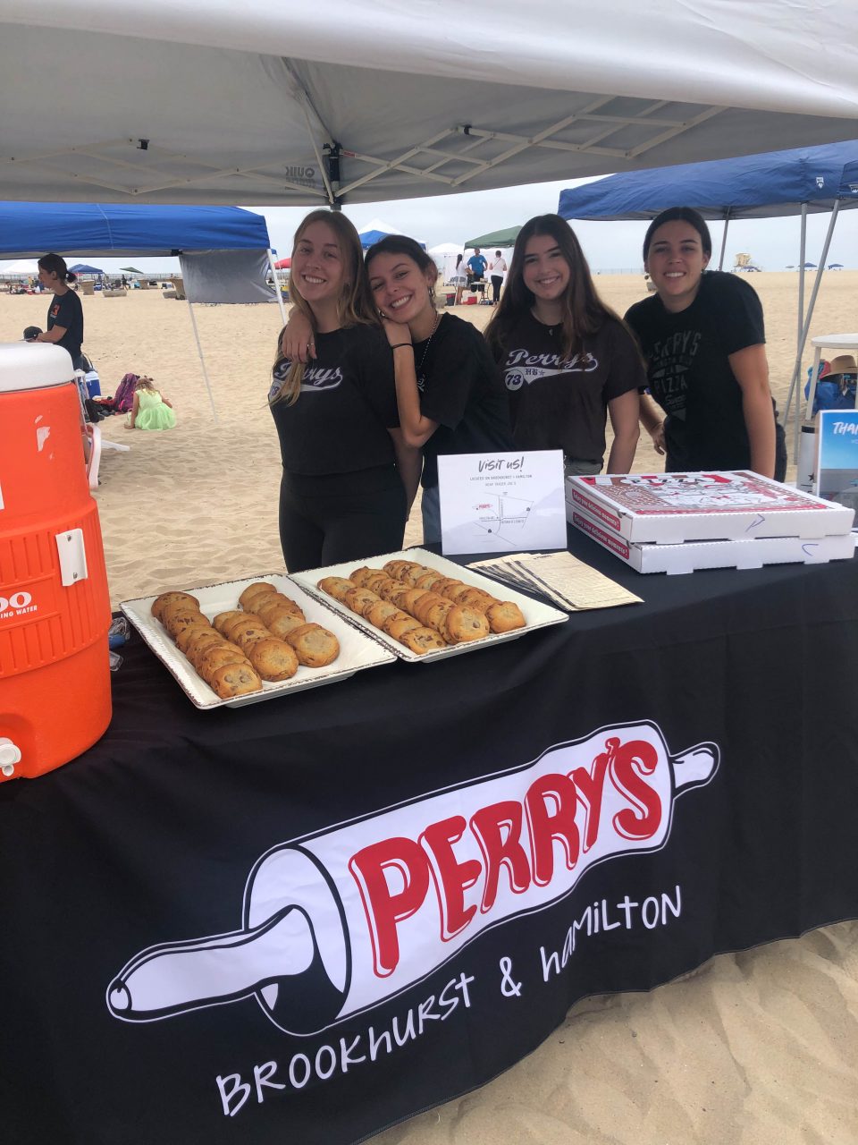 group of employees pass out cookies underneath an ez up a a beach clean up event on the sand