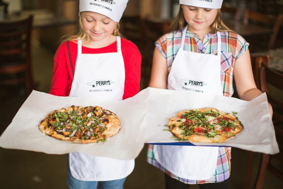 two children in aprons and chef hats hold small pizzas